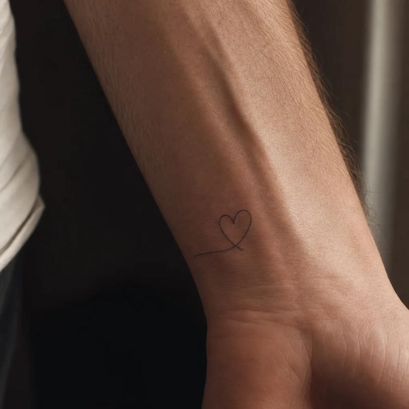 Tatouage petit cœur minimaliste en trait continu sur le poignet d'un homme