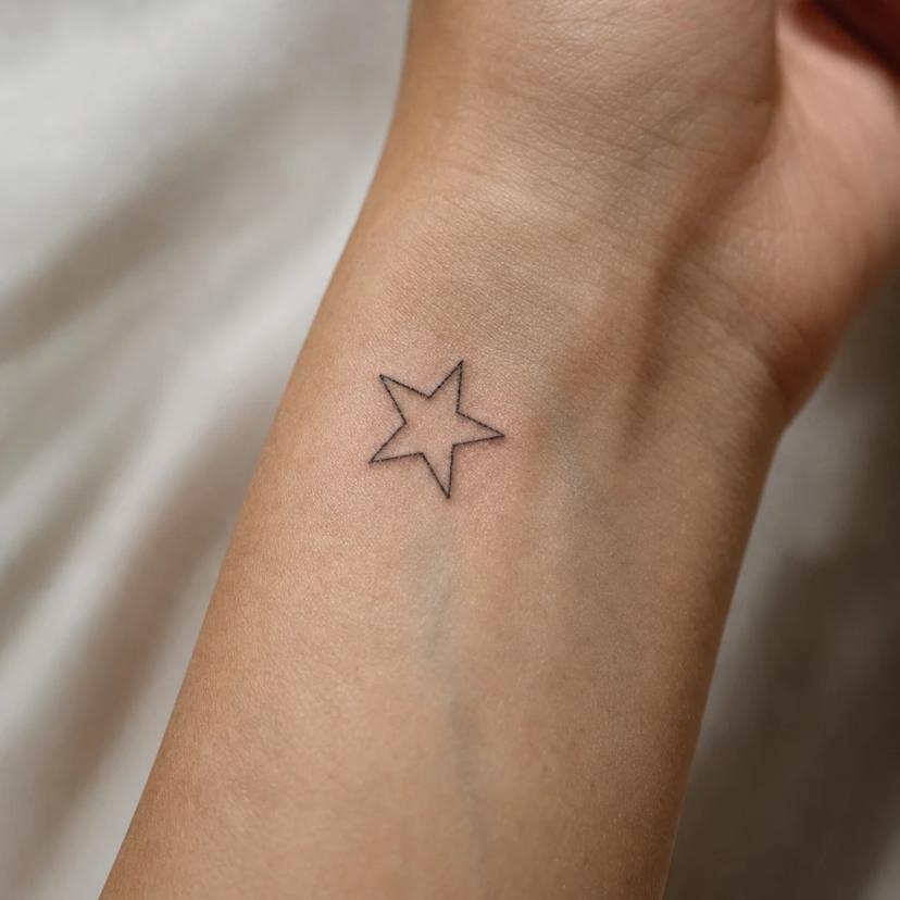 Tatouage étoile à cinq branches en contour fine-line sur le poignet d'une femme
