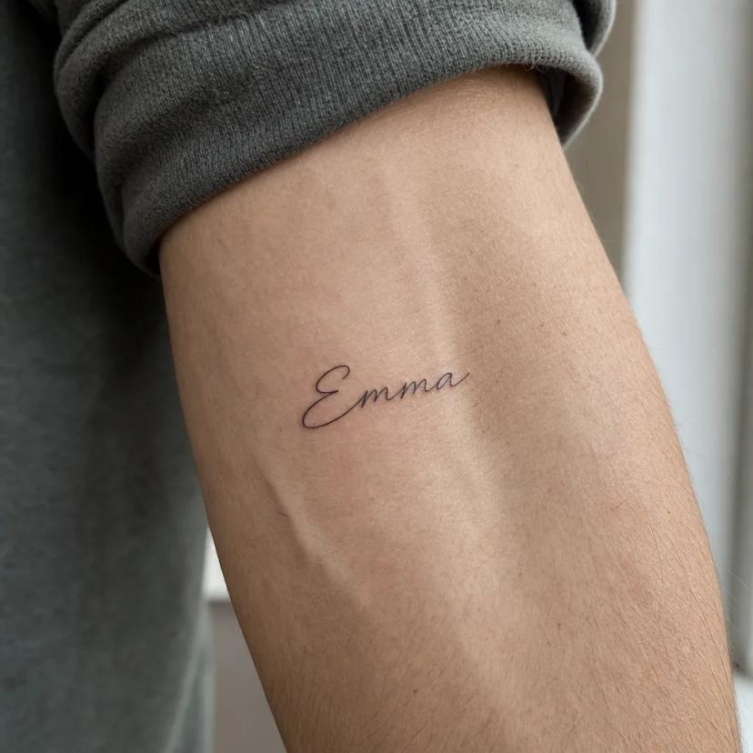 Prénom Emma tatoué en script fin sur l'avant-bras d'un homme, exemple typique de tatouage de couple qu'on regrette après une rupture